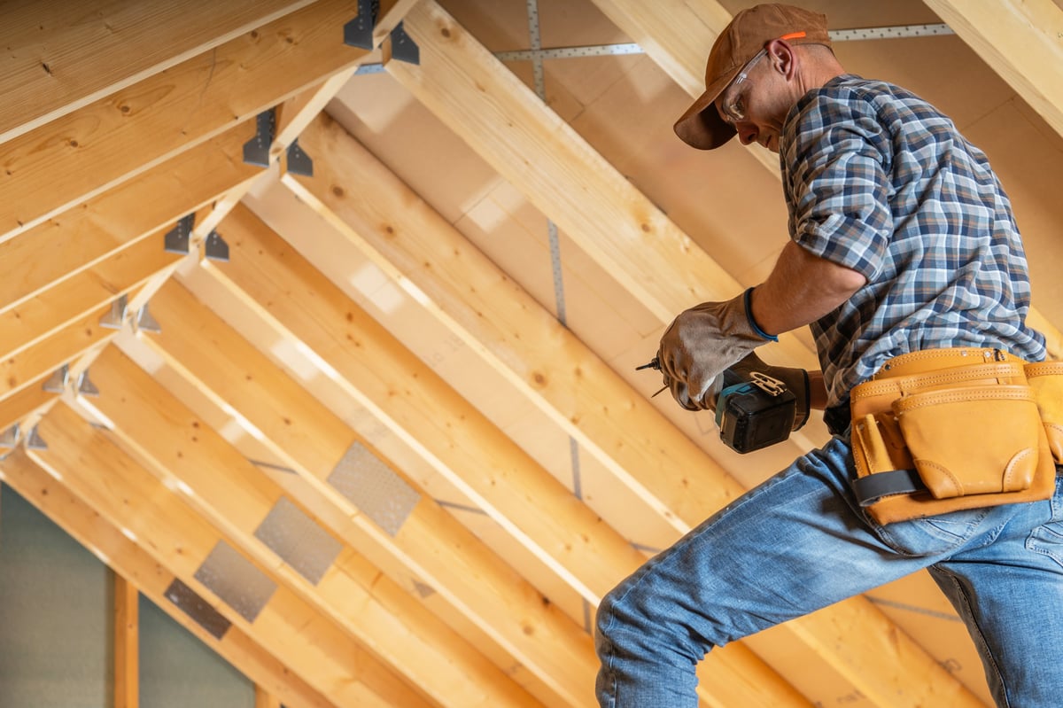 A specialist installing wooden structural beams in an attic during a home renovation